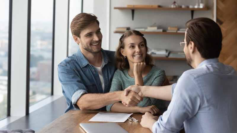 Happy loving married family couple shaking hands with Real Estate Agent